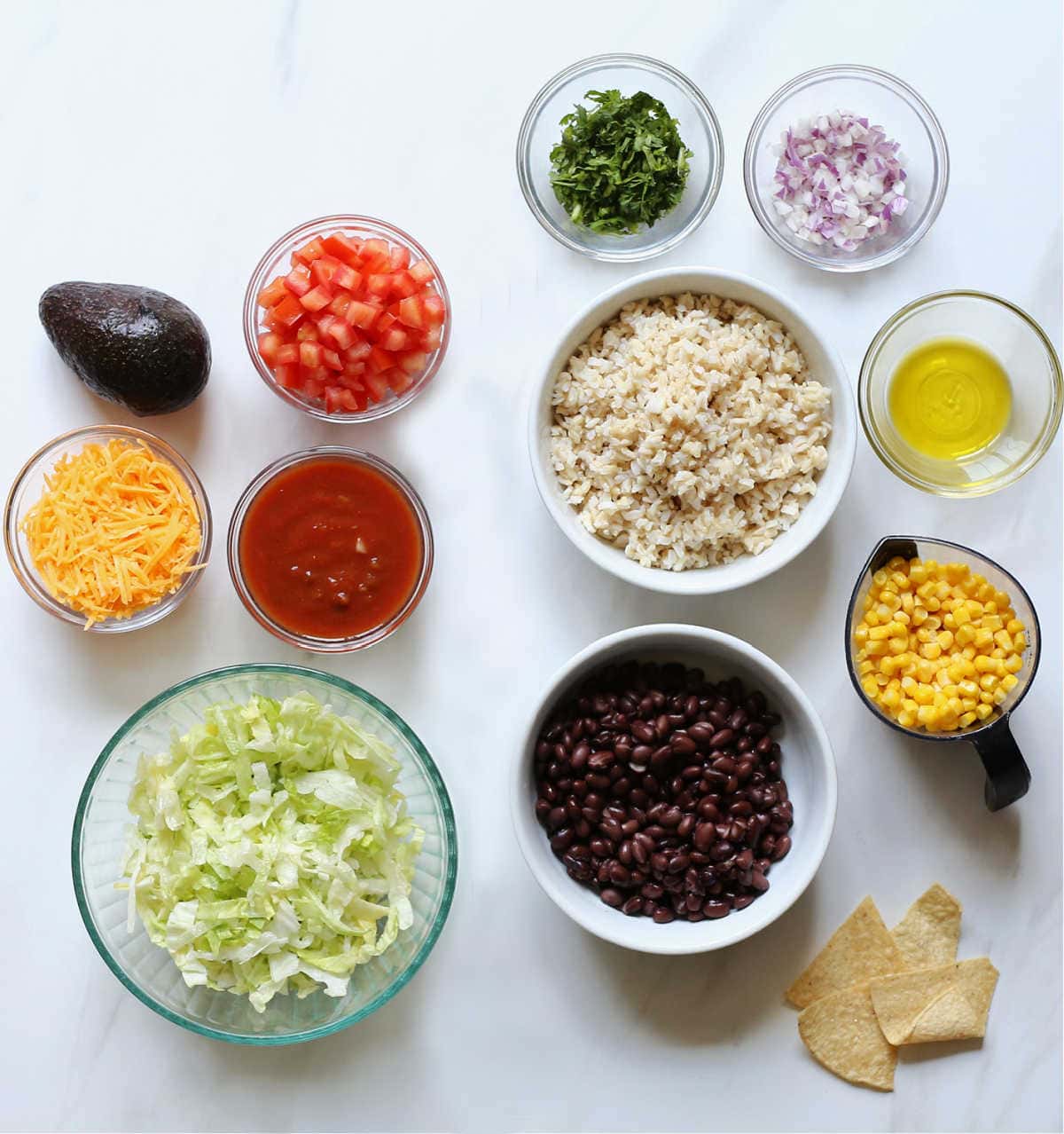 Vegetarian taco salad ingredients in bowls: black beans, rice, salsa, tomatoes, lettuce, cilantro, onion, chips.