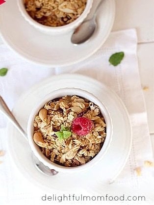 Granola served warm in a cup topped with a raspberry and mint.