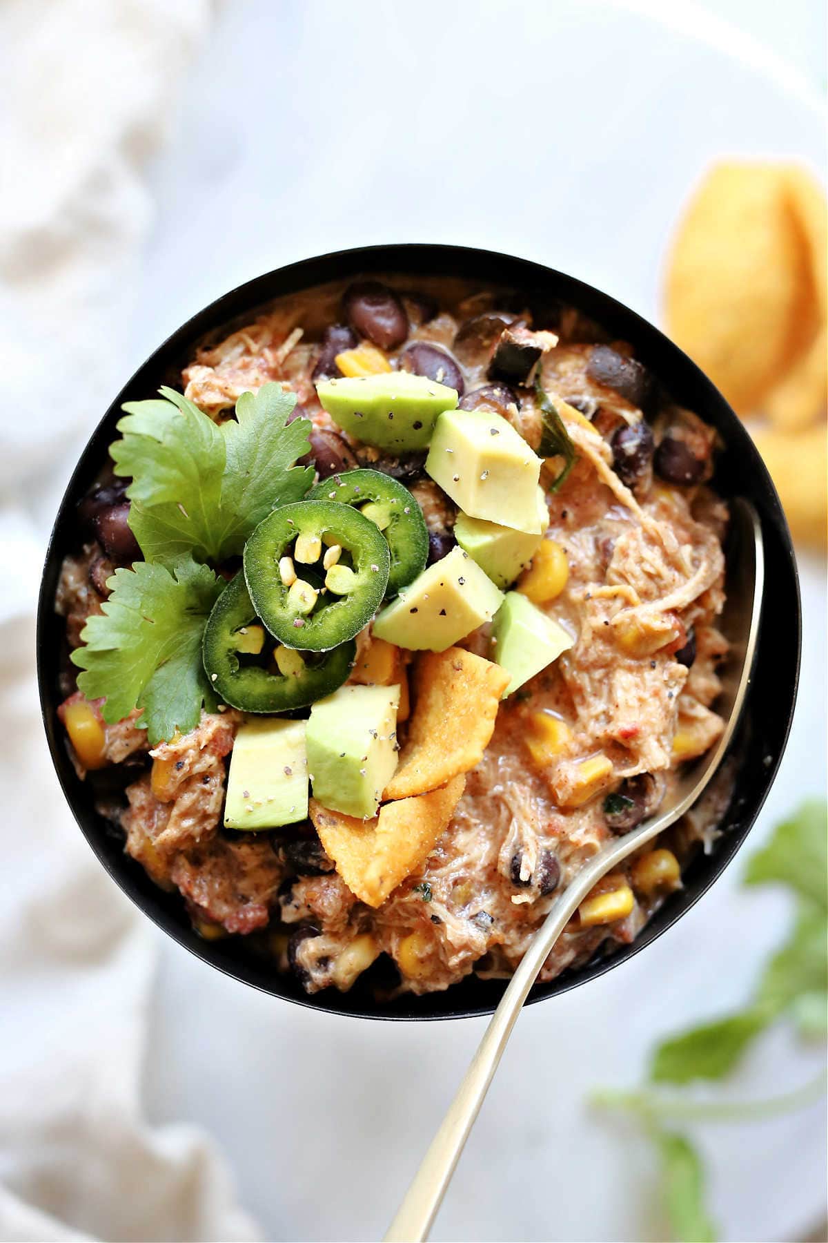 creamy taco chicken chili made with cream cheese cooked in a crockpot and served in a black bowl with a gold spoon