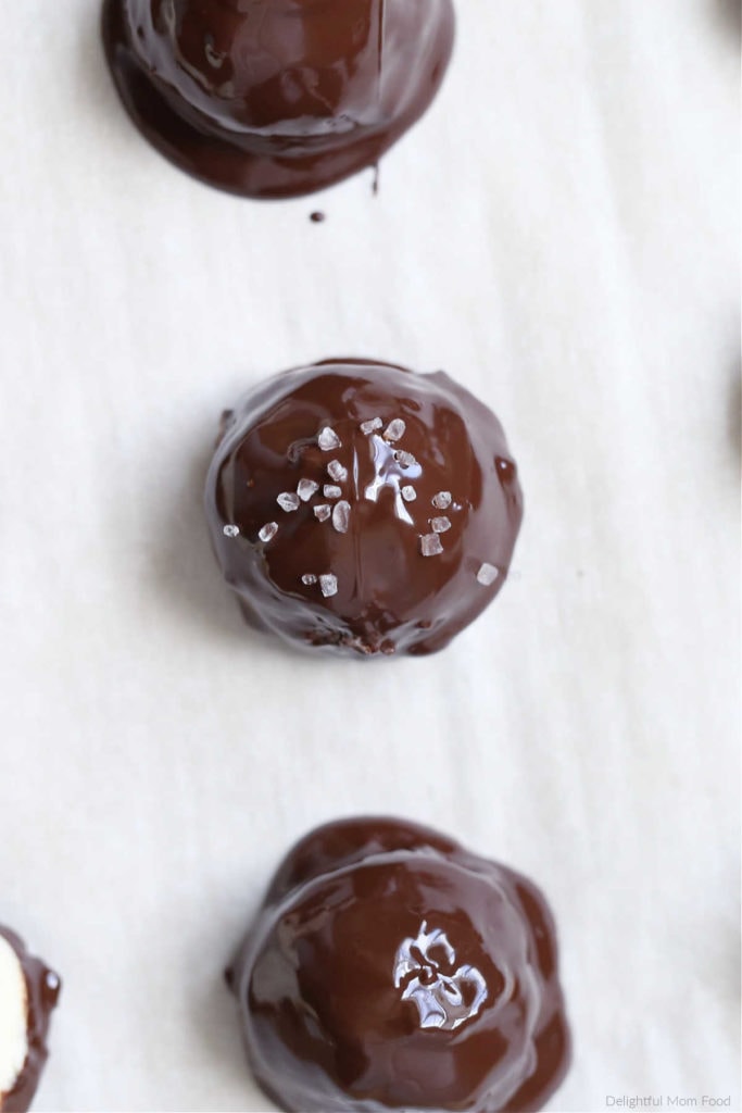 no-bake chocolate covered coconut ball recipe sprinkled with salt on top placed on a sheet pan for chocolate to cool