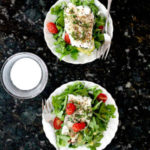 baked cod fish fillets over salad on two plates