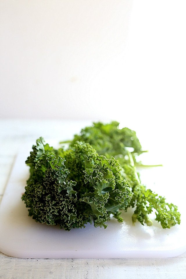 Bunch of fresh curly kale on a white cutting board ready to become kale chips.