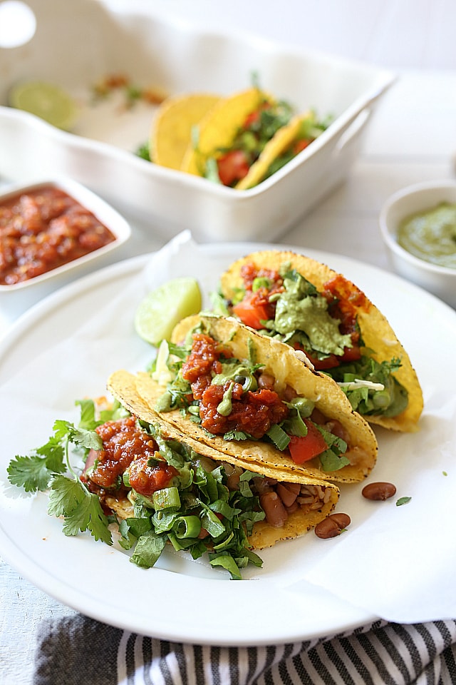 Mexican rice, beans, cheese, lettuce, cilantro and tomatoes stuffed into warm taco shells and topped with a creamy green vegan sauce. Super easy and healthy recipe for hard shell tacos in under 30 minutes!
