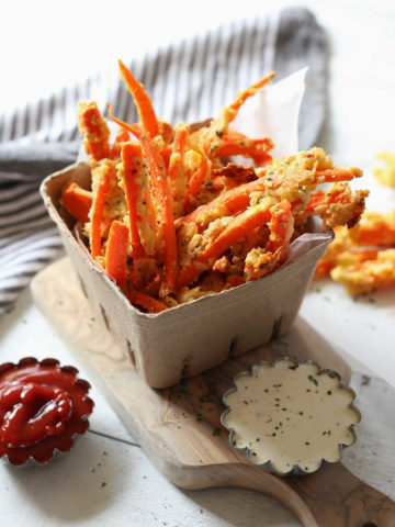 Carrot Fries in a cardboard cup on a cutting board served with ketchup and dressing