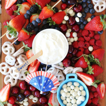 wood platter topped with strawberries cherries blueberries yogurt pretzels and yogurt dip for a simple red white blue theme for 4th of july