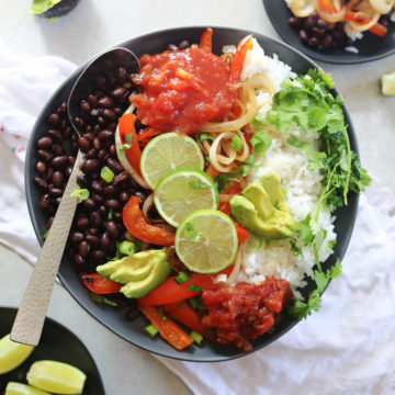 black bean vegetarian burrito bowl topped with avocado salsa cilantro and limes on a plate with a serving spoon