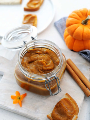 homemade pumpkin butter served in a jar with a slice of toast on a cutting board.