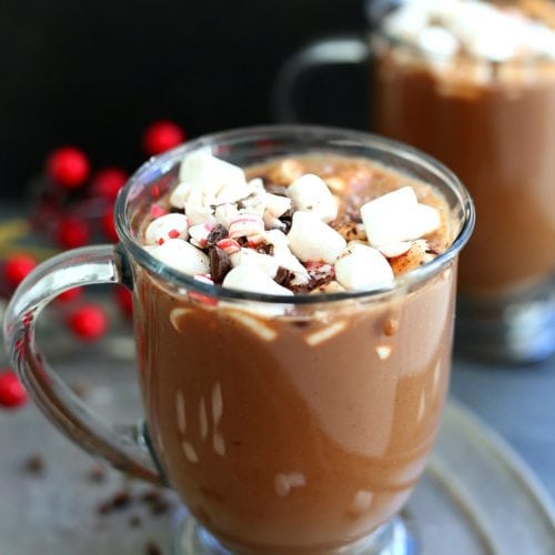 two mugs filled with the best vegan hot chocolate recipe topped with marshmallows, chocolate and peppermint bites
