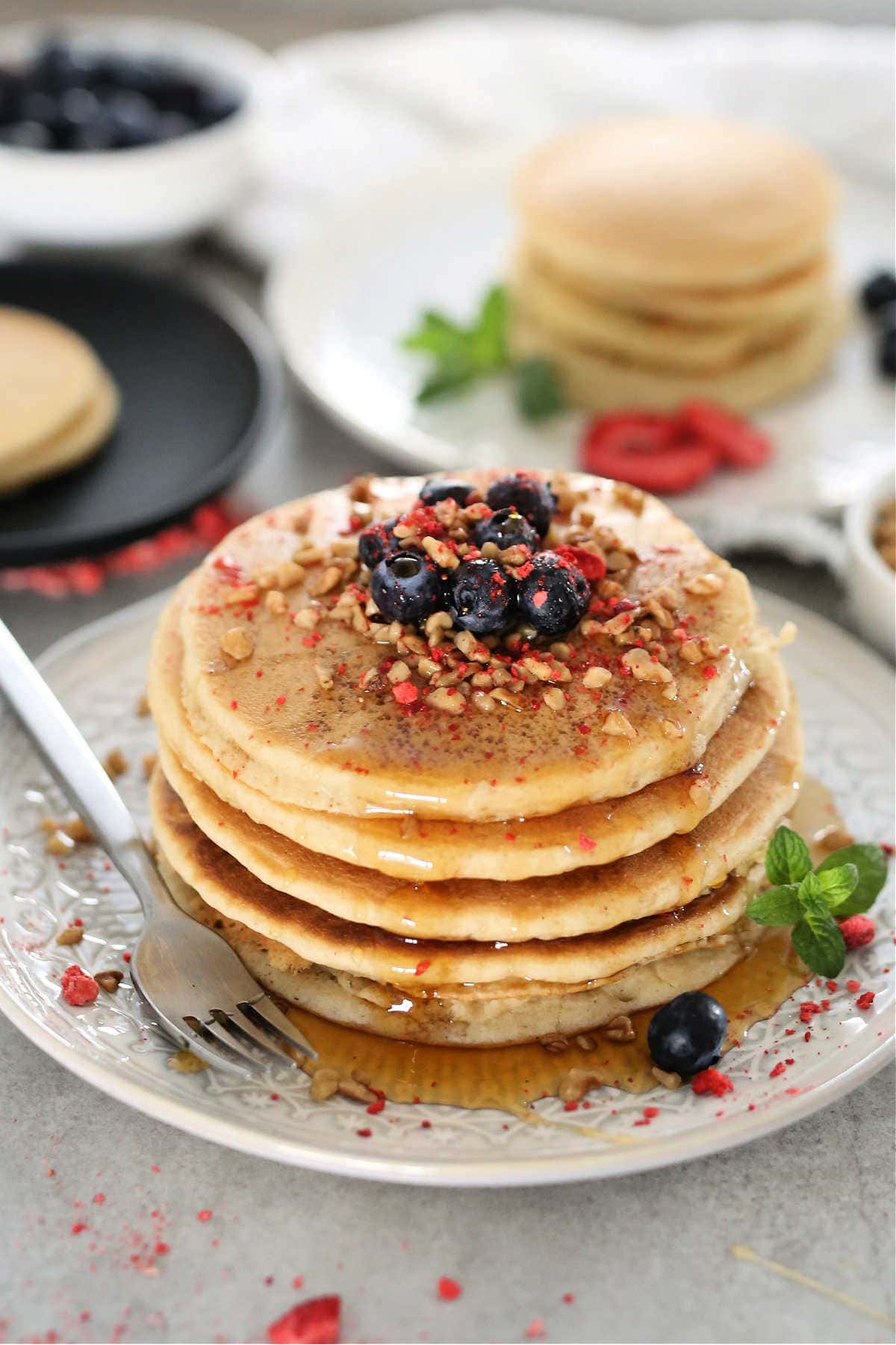 stack of fluffy paleo pancakes on a white plate with fruit on top