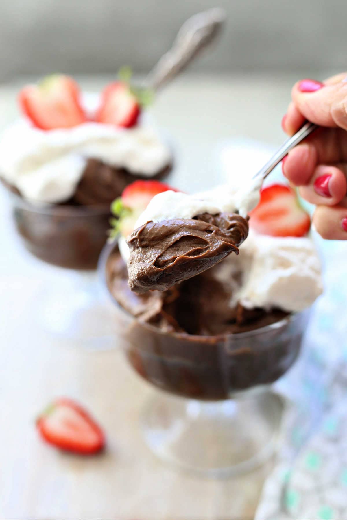 hand scooping with a spoon avocado chocolate pudding from a dessert glass bowl