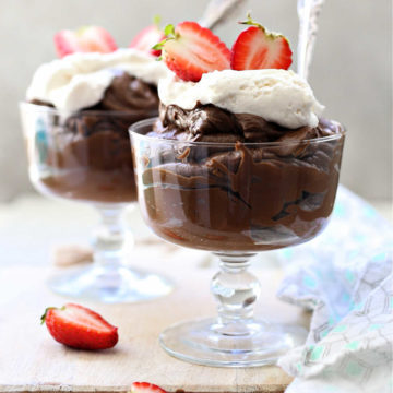 avocado chocolate pudding with whipped cream on top in a glass dessert bowl and strawberries on the side