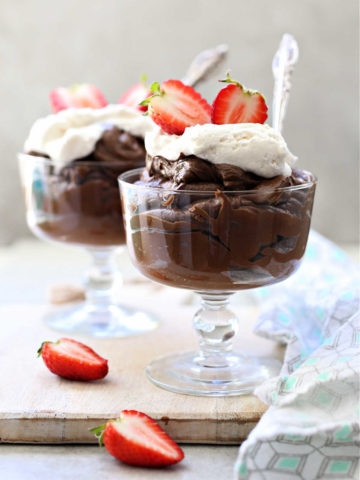 avocado chocolate pudding with whipped cream on top in a glass dessert bowl and strawberries on the side