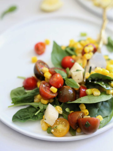 salad made with corn and tomatoes arugula basil and jicama in a light vinaigrette dressing served on a white platter