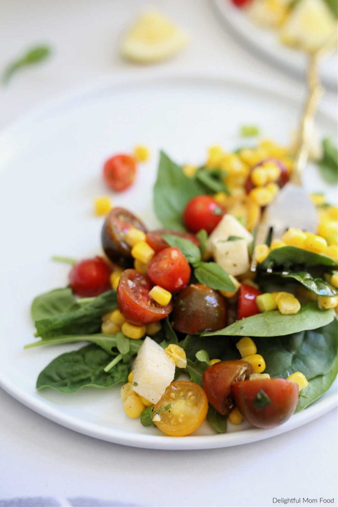 salad made with corn and tomatoes arugula basil and jicama in a light vinaigrette dressing served on a white platter