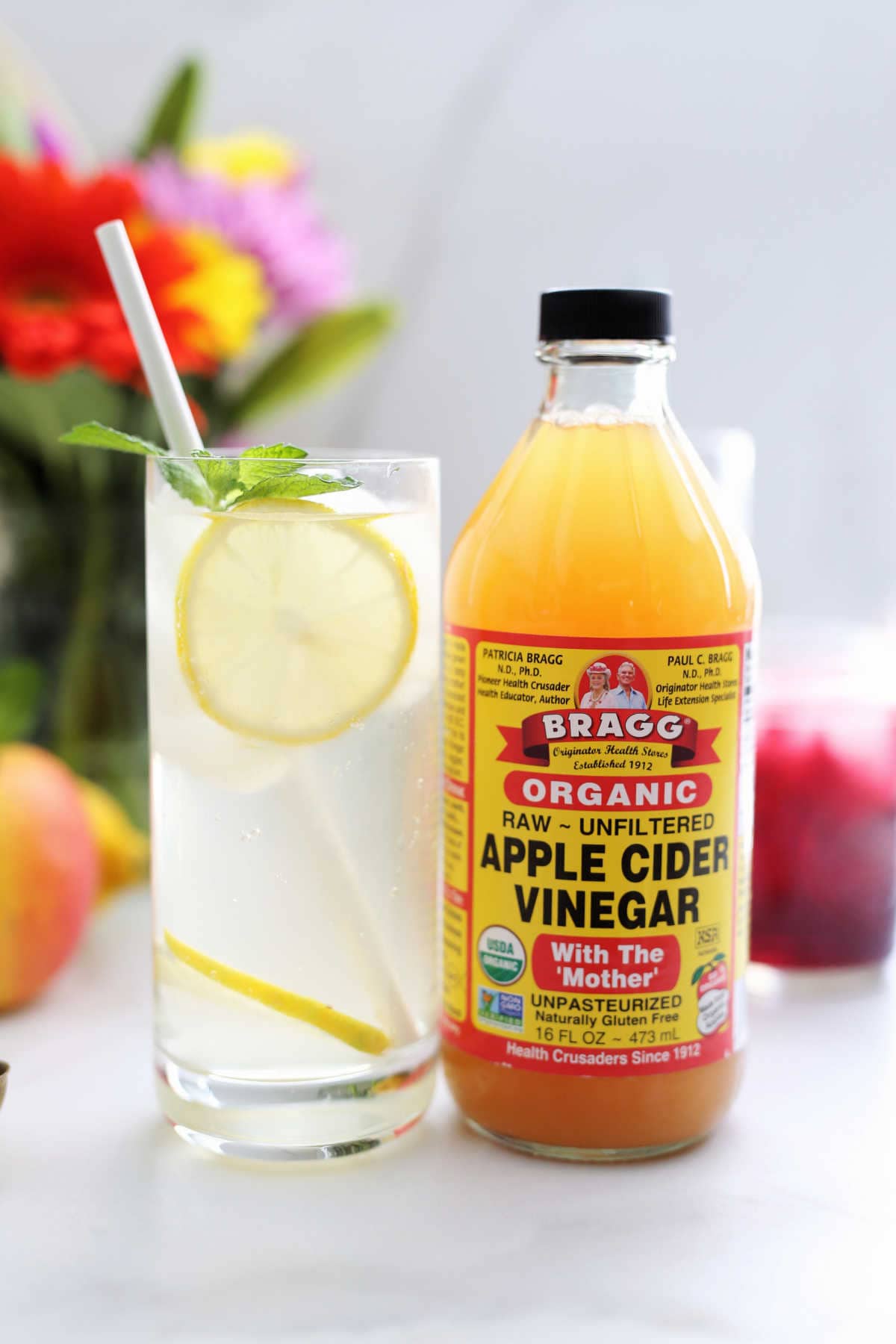 apple cider vinegar drink in a glass made with apple cider vinegar, water, lemon slices shown with a bottle of organic acv with the mother