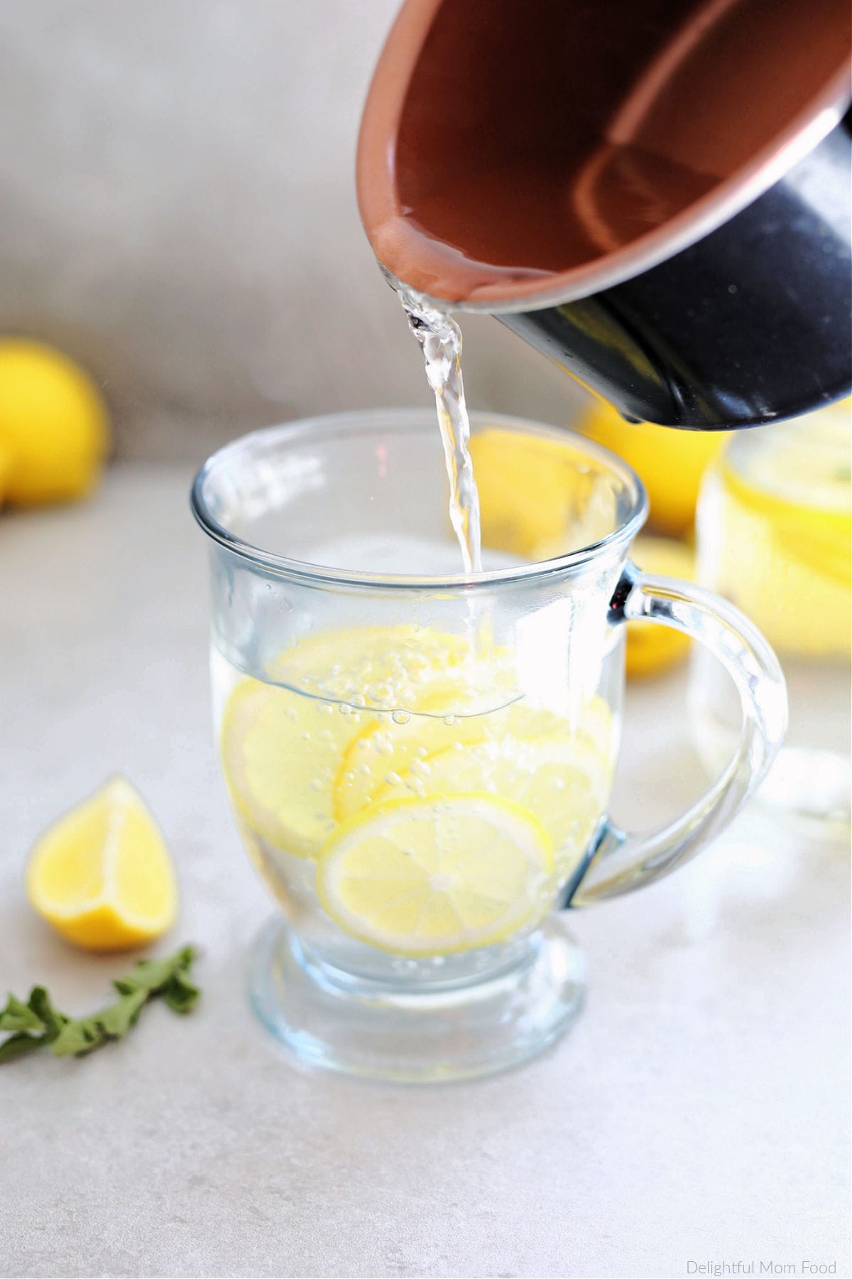 Saucepan pouring hot water over lemon juice and lemon citrus slices in a clear mug.