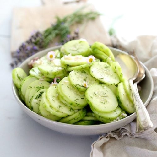 cucumber salad in a grey bowl served with serving spoons and lavender and dill in the background
