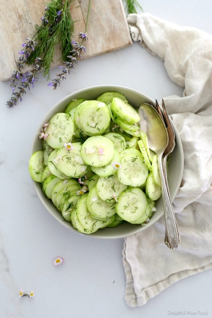 cucumbers sliced thin and turned into a salad served in a bowl with a serving spoon and dish towel next to it