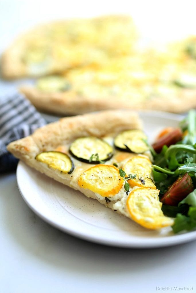 a slice of zucchini pizza served on a plate with a salad and placed by a dish towel