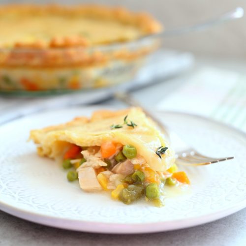 slice of gluten free chicken pot pie or turkey pot pie with fresh thyme on top and pie in the background