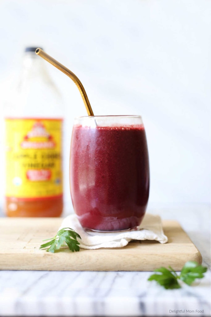 beauty detox and weight loss smoothie in a glass with a straw and a bottle of apple cider vinegar