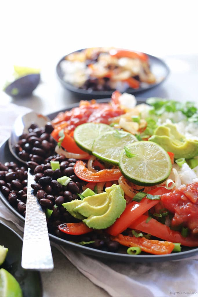 veggie burrito bowl with black beans, rice, peppers, onions on a plate with a serving spoon