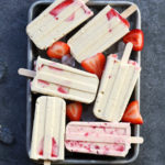 cheesecake popsicles on a tray with strawberries and ice