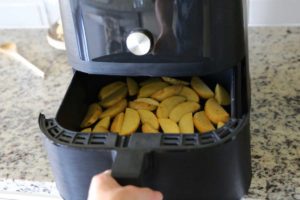 Hand closing air fryer basket to cook potato wedges.