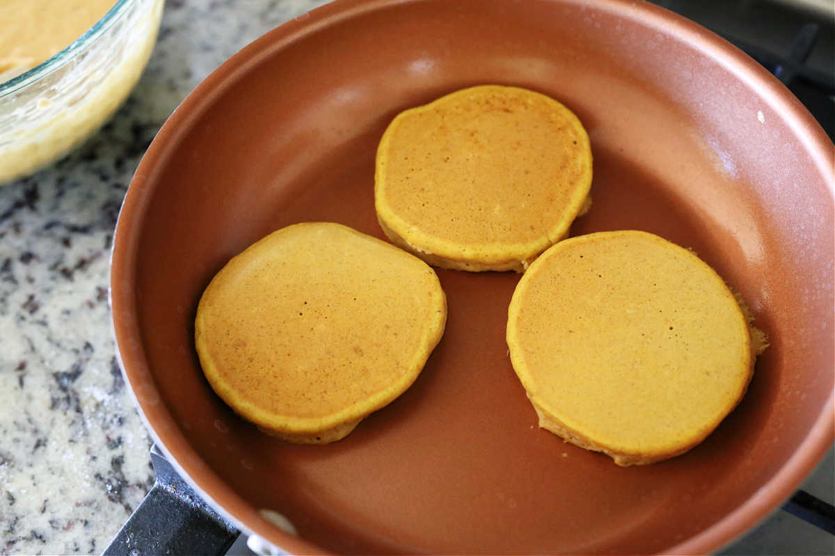 three pumpkin pancakes cooking on the stove