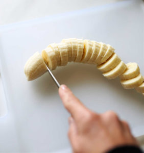 hand using a knife to slice bananas for freezing