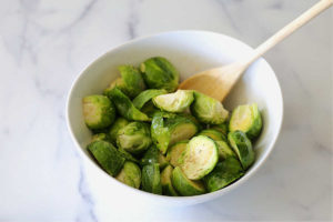 tossing brussels sprouts with olive oil, salt, and pepper in a bowl with a wood spoon
