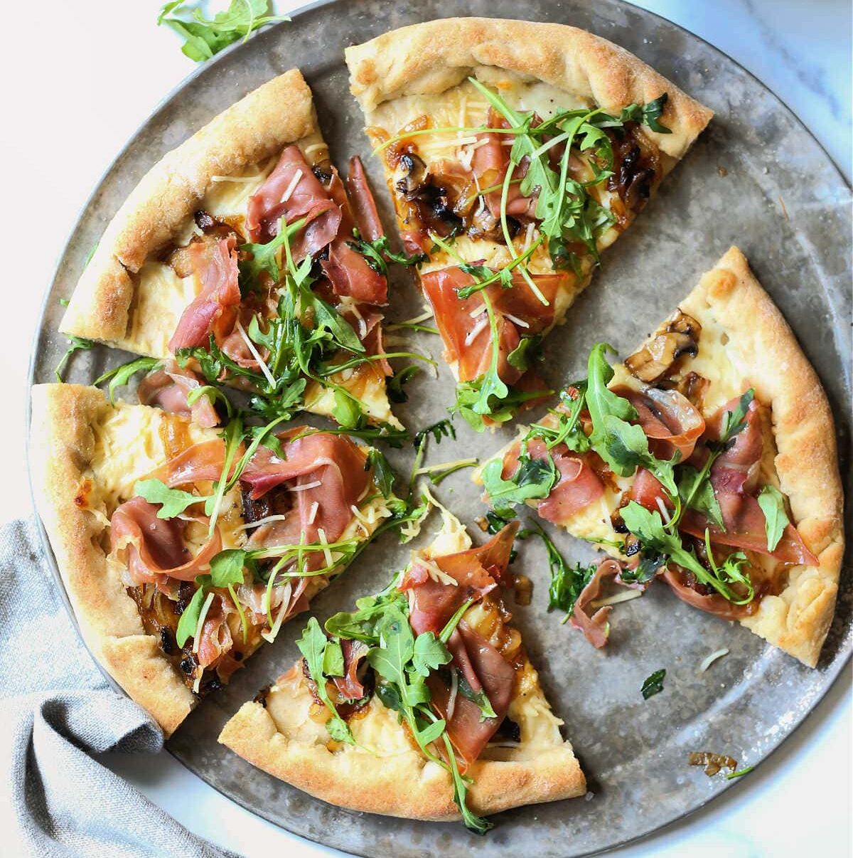 Arugula topped on a slice of gluten free pizza with prosciutto and caramel onion.