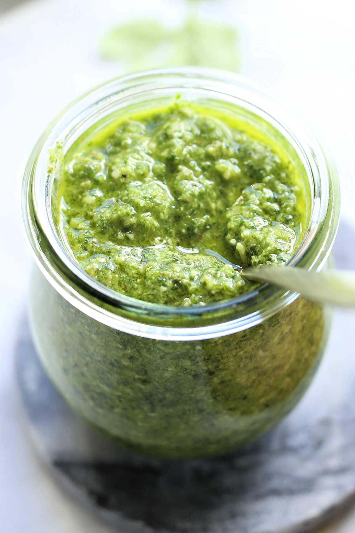 basil cilantro pesto in a glass jar with a serving spoon