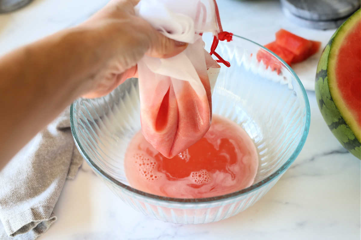 squeezing fresh homemade watermelon juice through a mesh bag into a bowl to strain the pulp