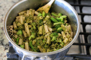 mixing pasta in a saucepan with cilantro and basil pesto, reserved water and broccoli florets