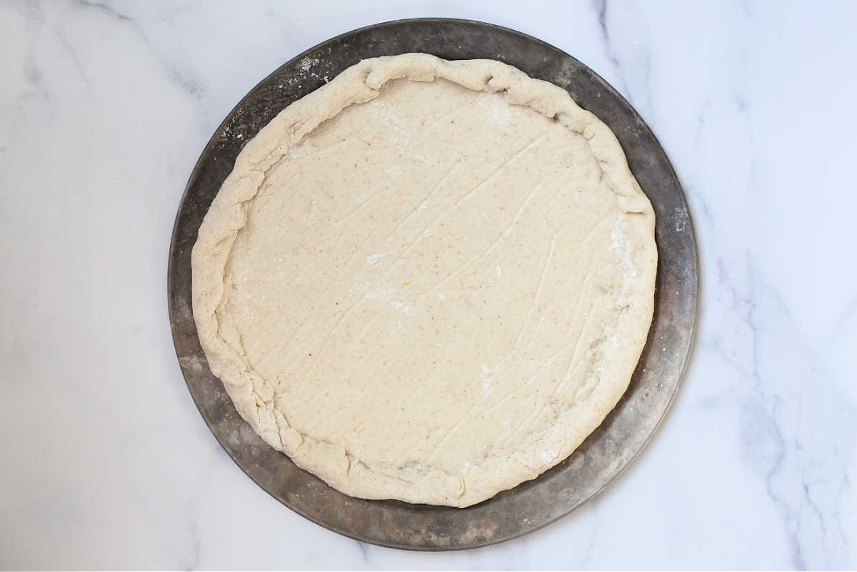 Gluten free pizza dough rolled out on a pizza pan for baking.