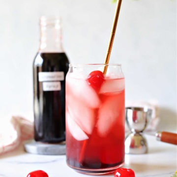 shirley temple drink in a glass with cherries and and a bottle of homemade grenadine syrup