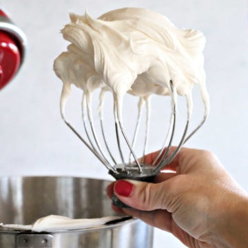 hand holding a whisk from an electric mixer with cream cheese buttercream frosting on it