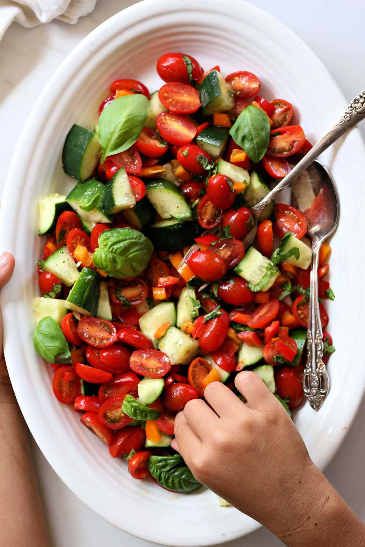 hand reaching of a salad made of cucumbers tomatoes and basil leaves