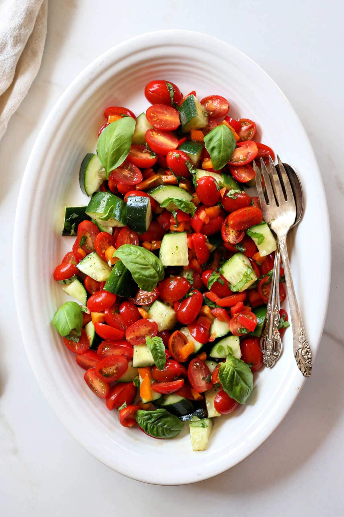 cucumber tomato salad recipe on a platter with serving fork and spoon