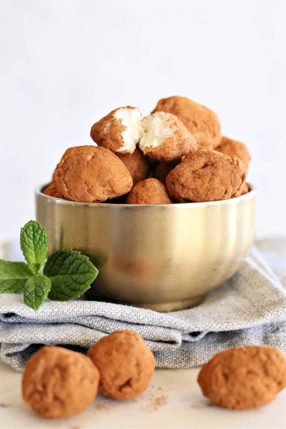 balls of homemade irish potato candy in a gold bowl on a towel with fresh mint