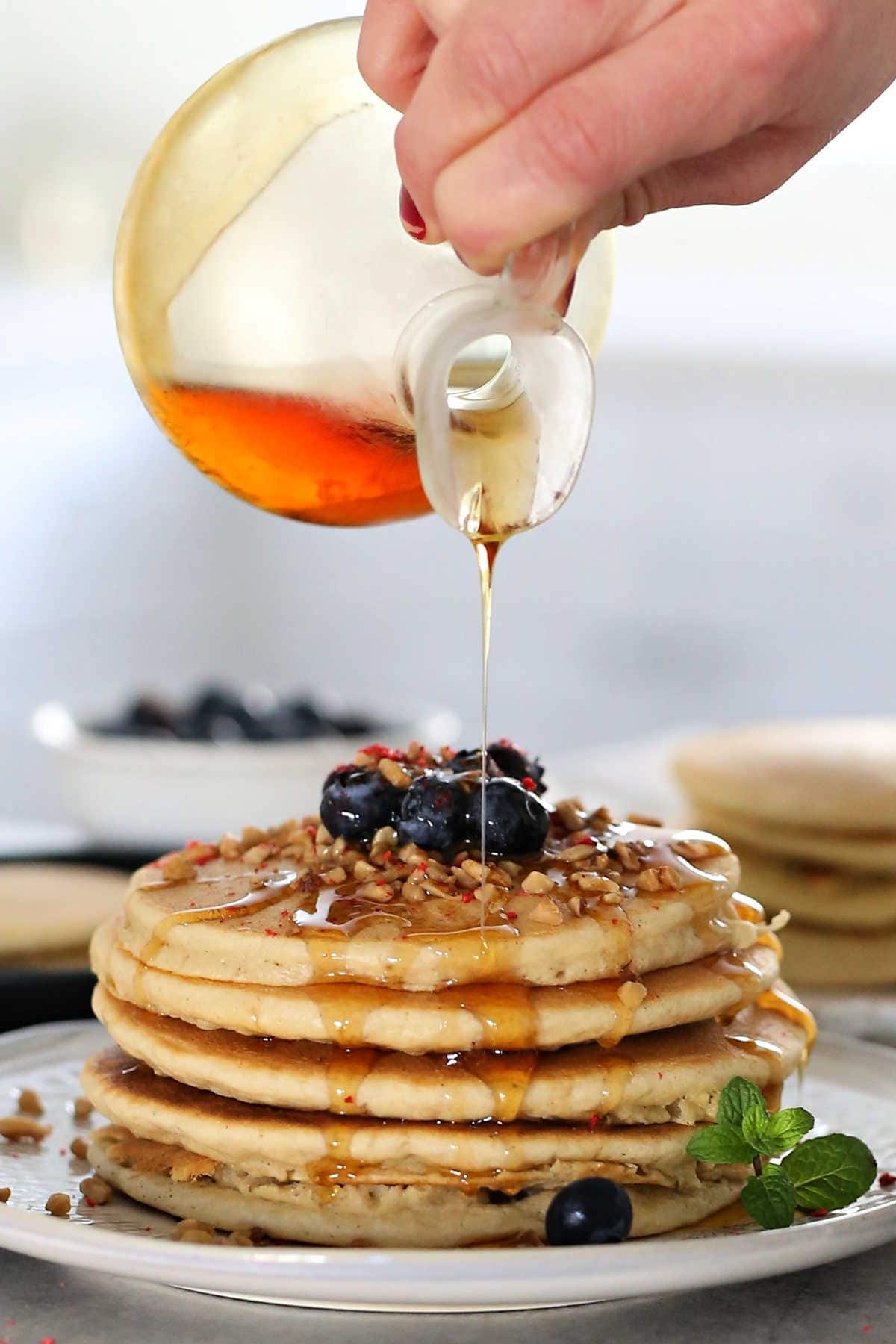 Pouring maple syrup over a stack of pancakes.