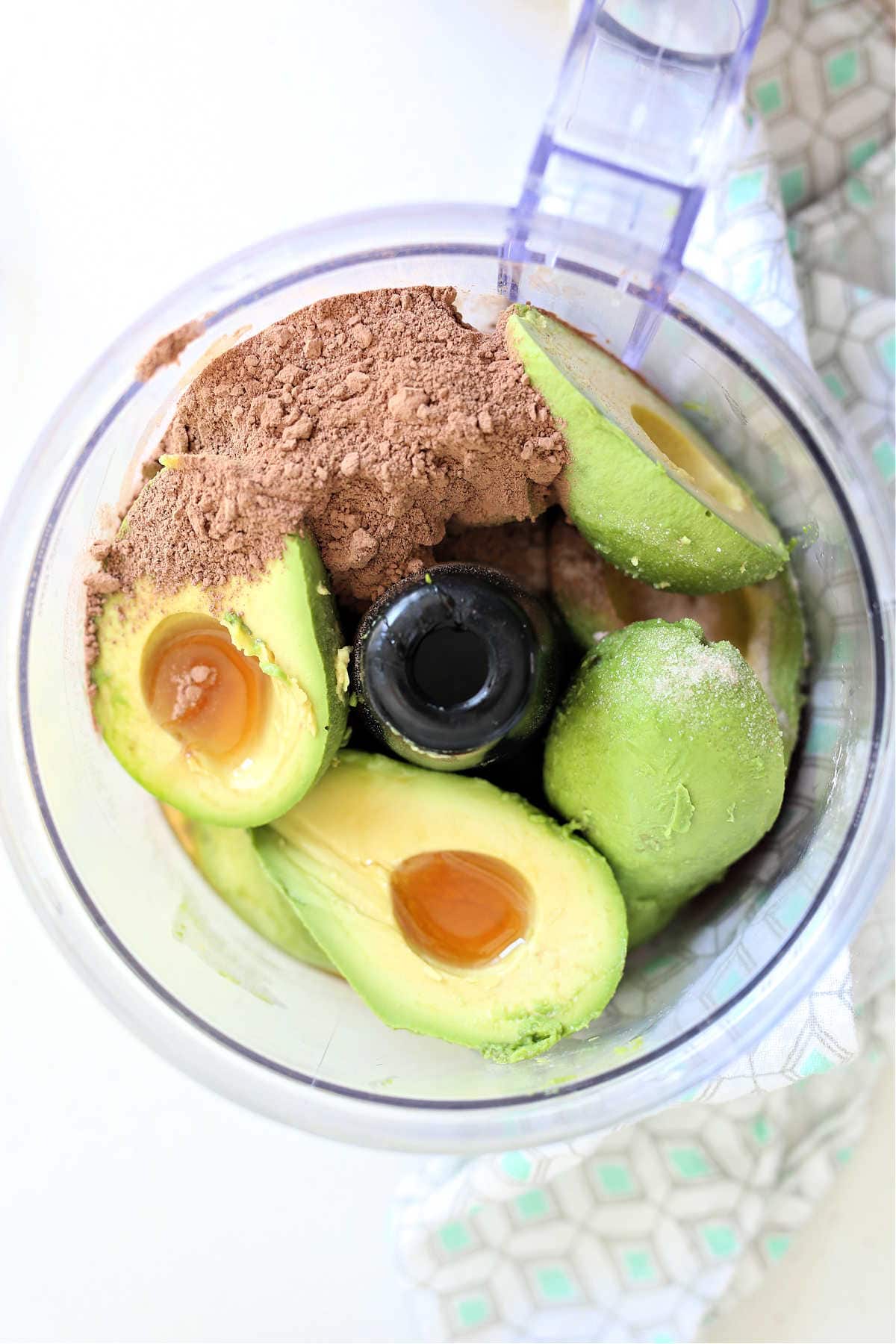 ingredients of avocados, cocoa powder, maple syrup, vanilla and salt in a food processor