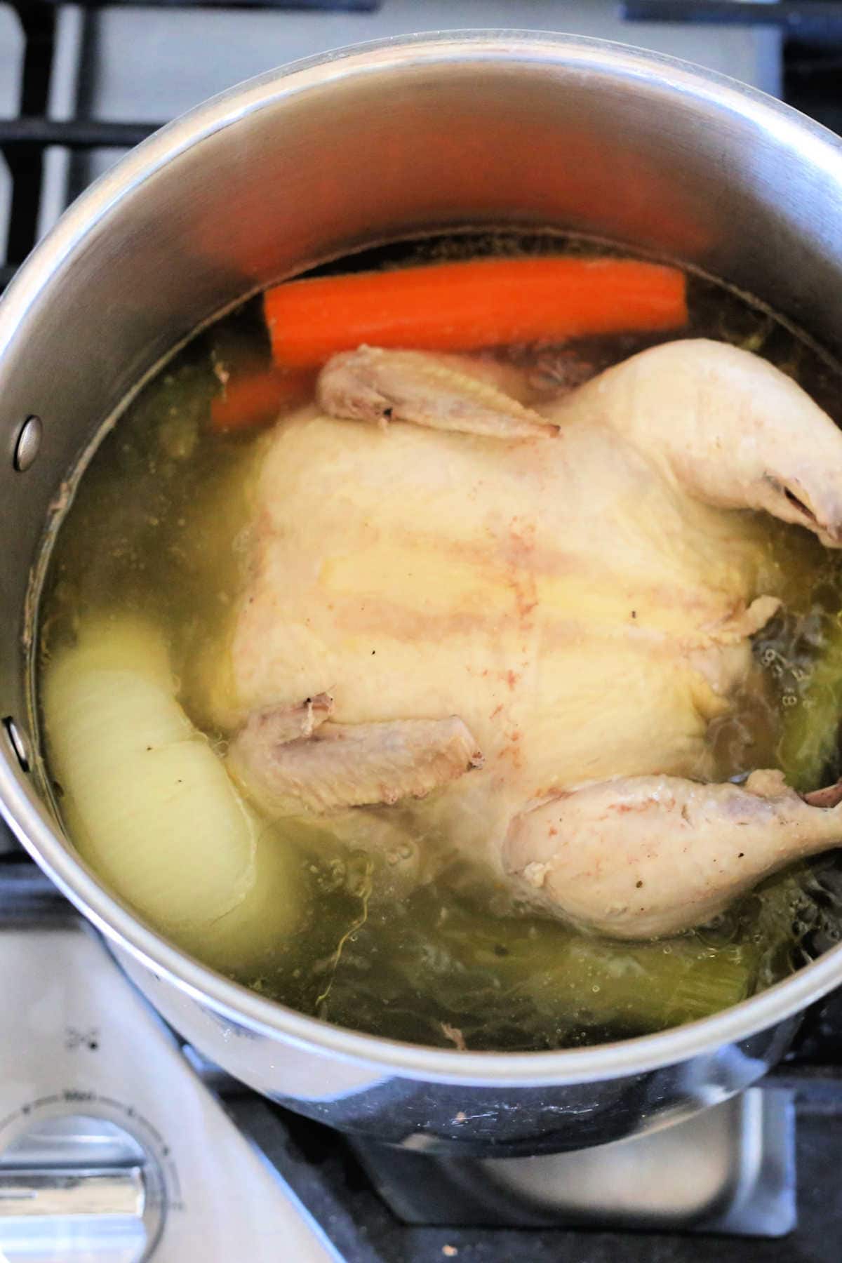 whole chicken cooking in a stockpot on the stove for broth
