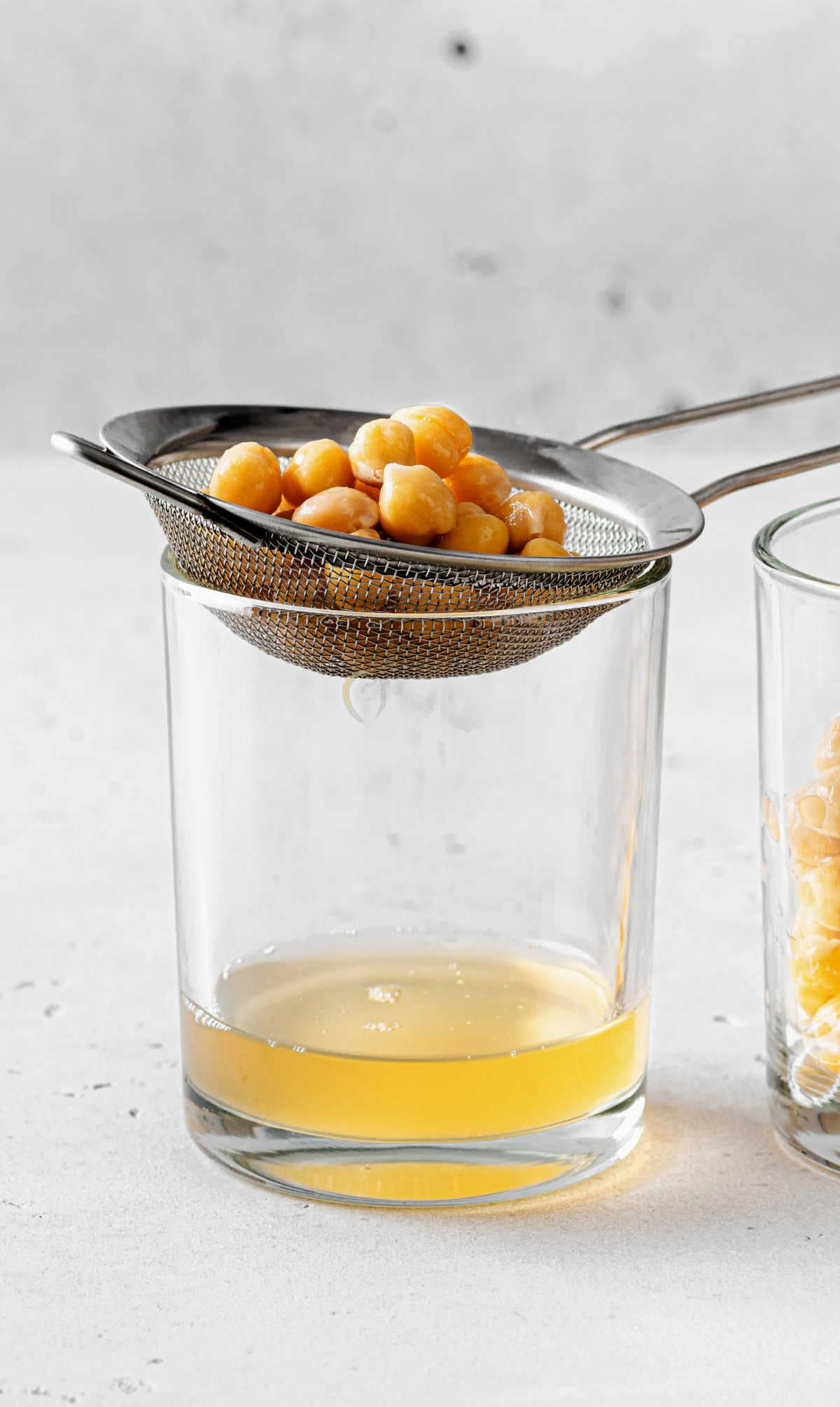 How To Make Aquafaba by straining cooked chickpeas over a glass to remove the aquafaba liquid