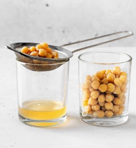 straining cooked chickpeas over a glass to separate the aquafaba liquid