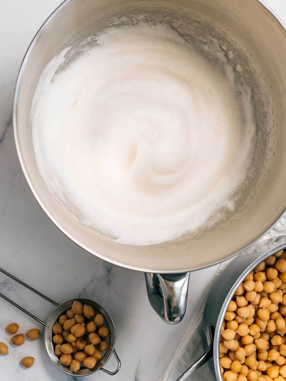 whipped aquafaba in a mixing bowl with cooked chickpeas next to it