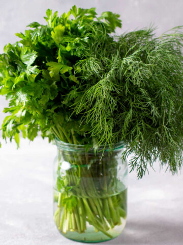 fresh herbs stored in a glass jar with water