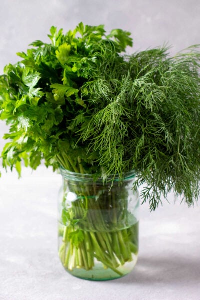 fresh herbs stored in a glass jar with water