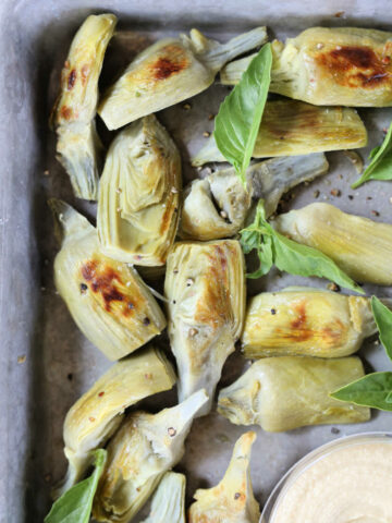 Roasted Artichokes on a baking pan with fresh basil leaves